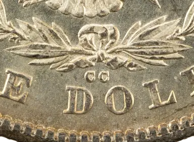 A close view of the bottom of the back of a Morgan dollar: two small letters C side by side below the bow of the wreath, just above the D and O of the word DOLLAR.